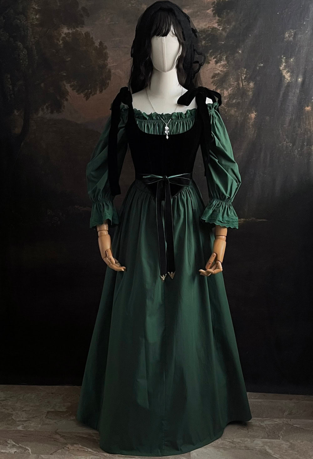 A historical fashion inspired outfit consisting of a forest green chemise a la reine style dress with bell sleeves, a black velvet corset, a green velvet belt, and silver jewelry.