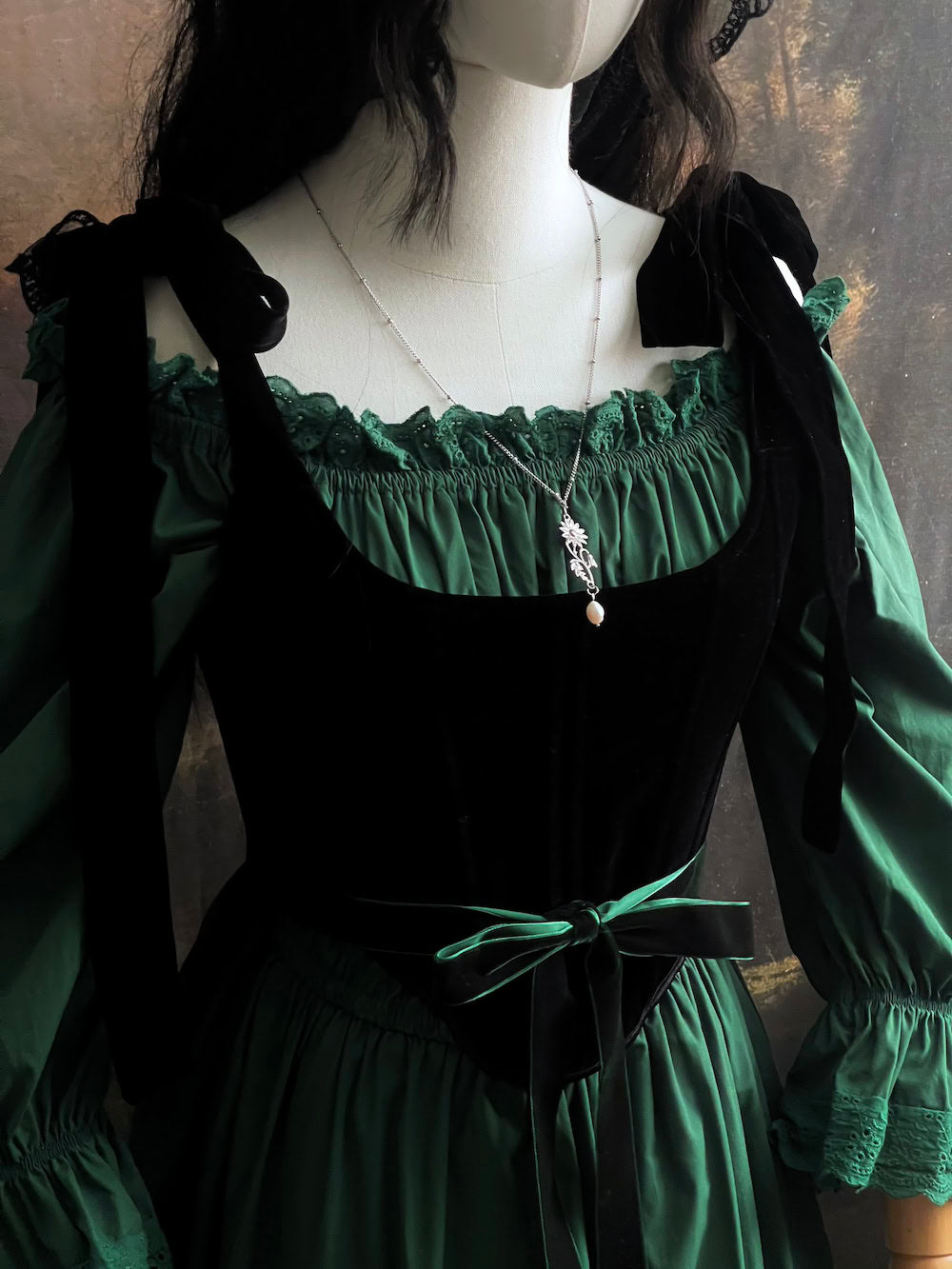 A mannequin wearing an outfit inspired by historical fashion, consisting of a green ruched dress with lace trim, a green velvet belt, and gothic black velvet corset.