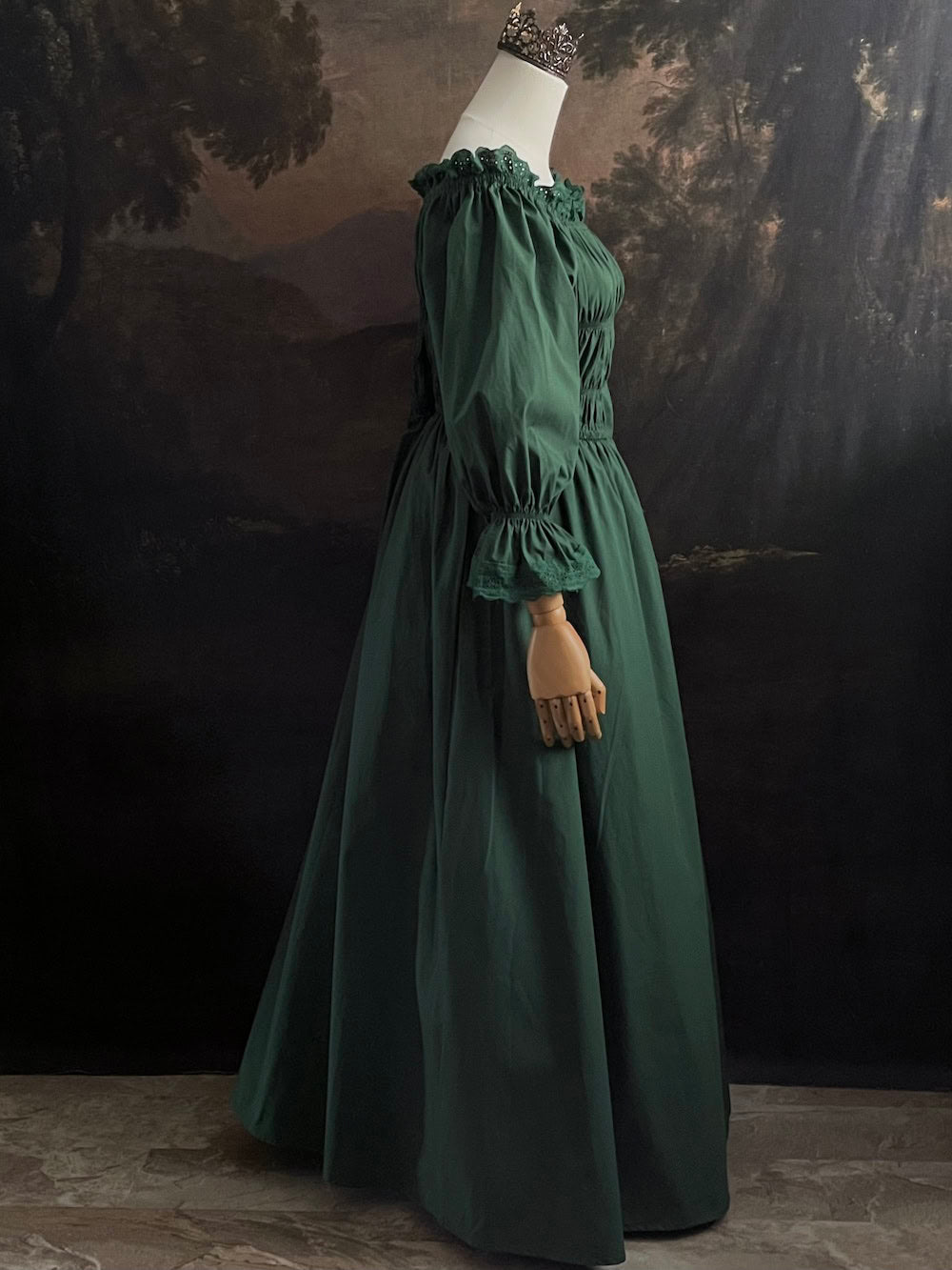 Dark Forest Green historical fashion inspired shirred chemise maxi dress gown with lace trim and bell sleeves on a mannequin against a dark forest background
