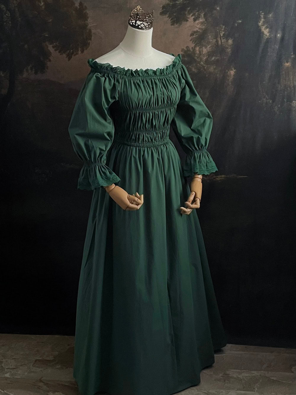 Dark Forest Green historical fashion inspired shirred chemise maxi dress gown with lace trim and bell sleeves on a mannequin against a dark forest background