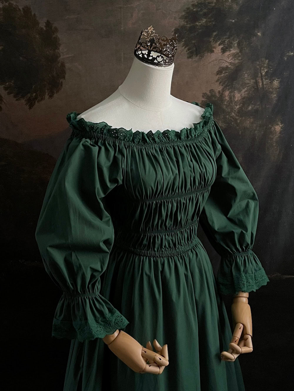 Dark Forest Green historical fashion inspired shirred chemise maxi dress gown with lace trim and bell sleeves on a mannequin against a dark forest background