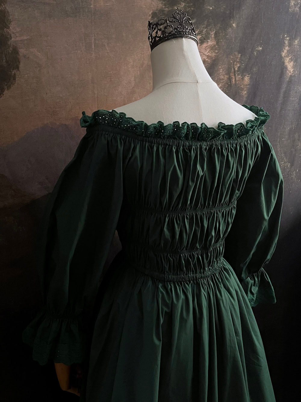 Dark Forest Green historical fashion inspired shirred chemise maxi dress gown with lace trim and bell sleeves on a mannequin against a dark forest background