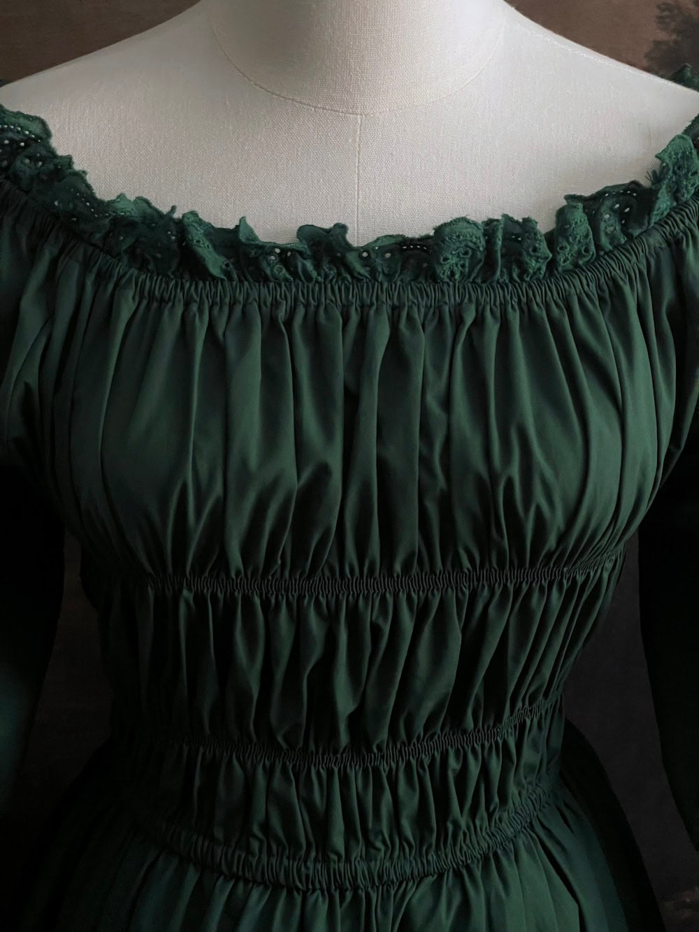 Dark Forest Green historical fashion inspired shirred chemise maxi dress gown with lace trim and bell sleeves on a mannequin against a dark forest background