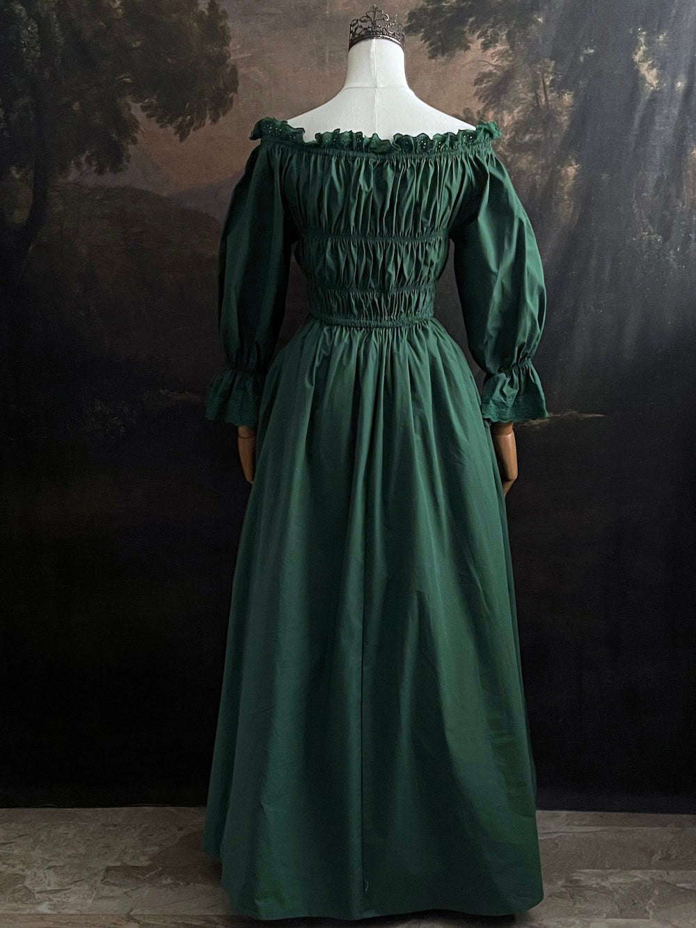Dark Forest Green historical fashion inspired shirred chemise maxi dress gown with lace trim and bell sleeves on a mannequin against a dark forest background