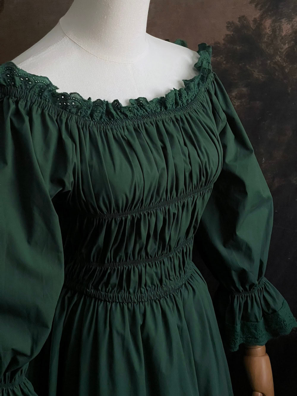 Dark Forest Green historical fashion inspired shirred chemise maxi dress gown with lace trim and bell sleeves on a mannequin against a dark forest background