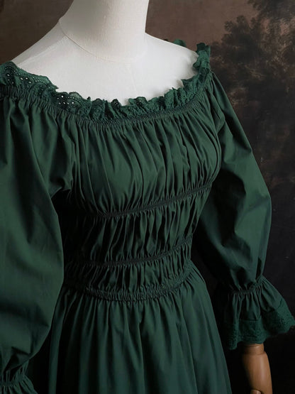 Dark Forest Green historical fashion inspired shirred chemise maxi dress gown with lace trim and bell sleeves on a mannequin against a dark forest background