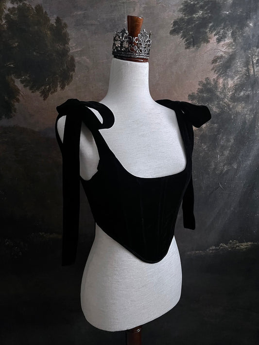 A pair of historical fashion inspired renaissance and baroque era gothic black velvet corset stays with bow straps, a basque waist, and a square neckline.