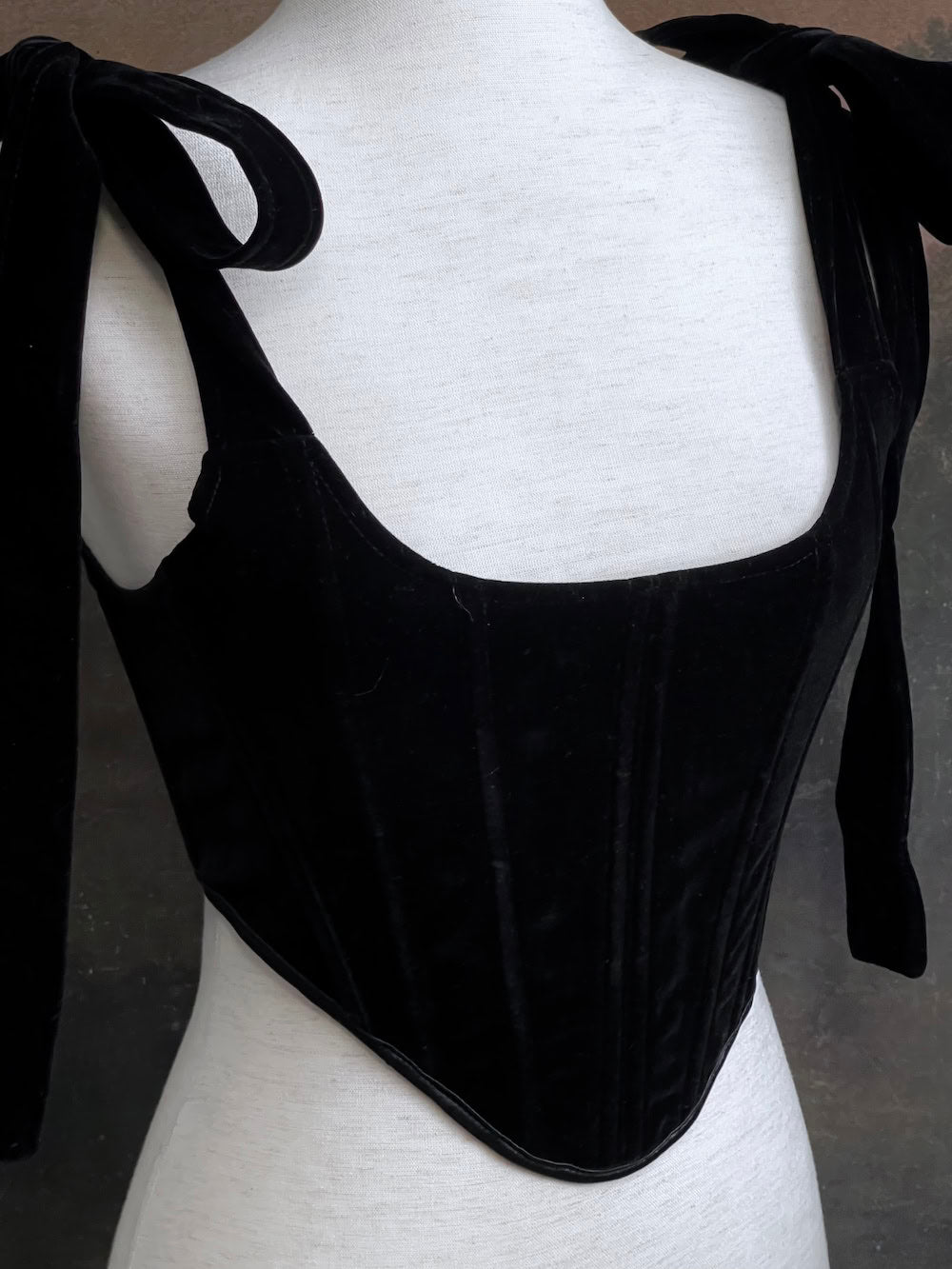 A pair of historical fashion inspired renaissance and baroque era gothic black velvet corset stays with bow straps, a basque waist, and a square neckline.