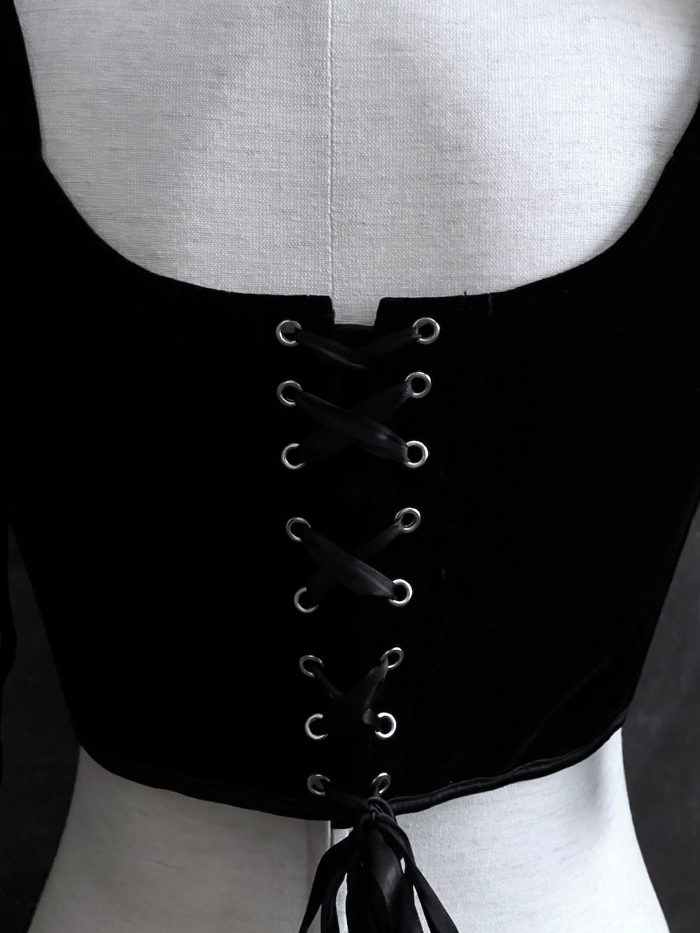 A pair of historical fashion inspired renaissance and baroque era gothic black velvet corset stays with bow straps, a basque waist, and a square neckline.