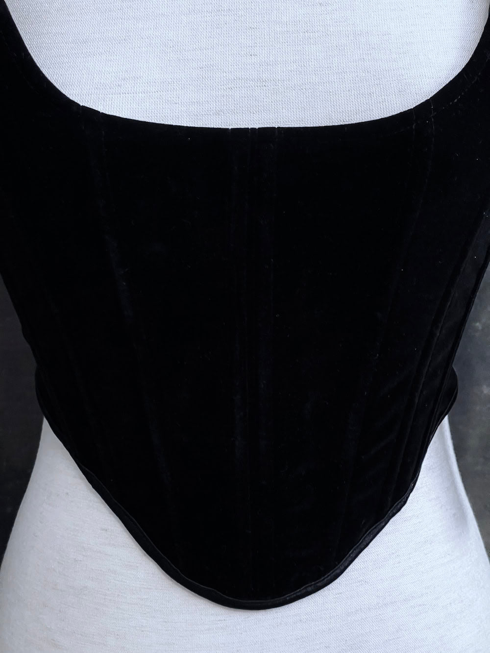 A pair of historical fashion inspired renaissance and baroque era gothic black velvet corset stays with bow straps, a basque waist, and a square neckline.