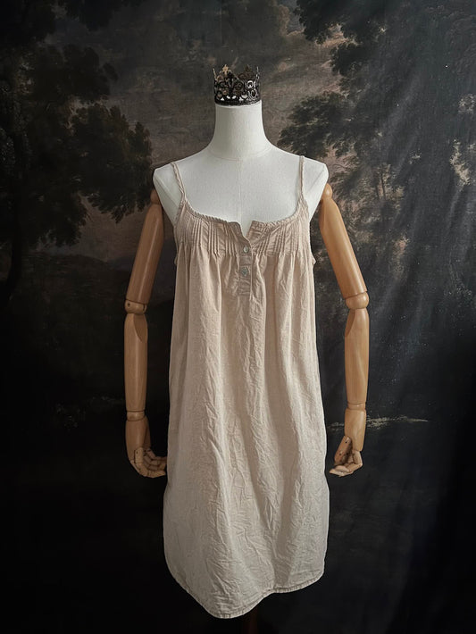 A HISTORICALLY INSPIRED Beige slip chemise dress on a mannequin against a historical painting backdrop.