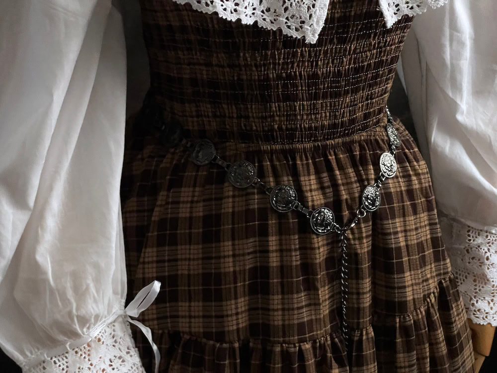 A historically inspired renaissance and medieval metal cameo coin belt in dark charcoal metal on a mannequin wearing a brown plaid dress.