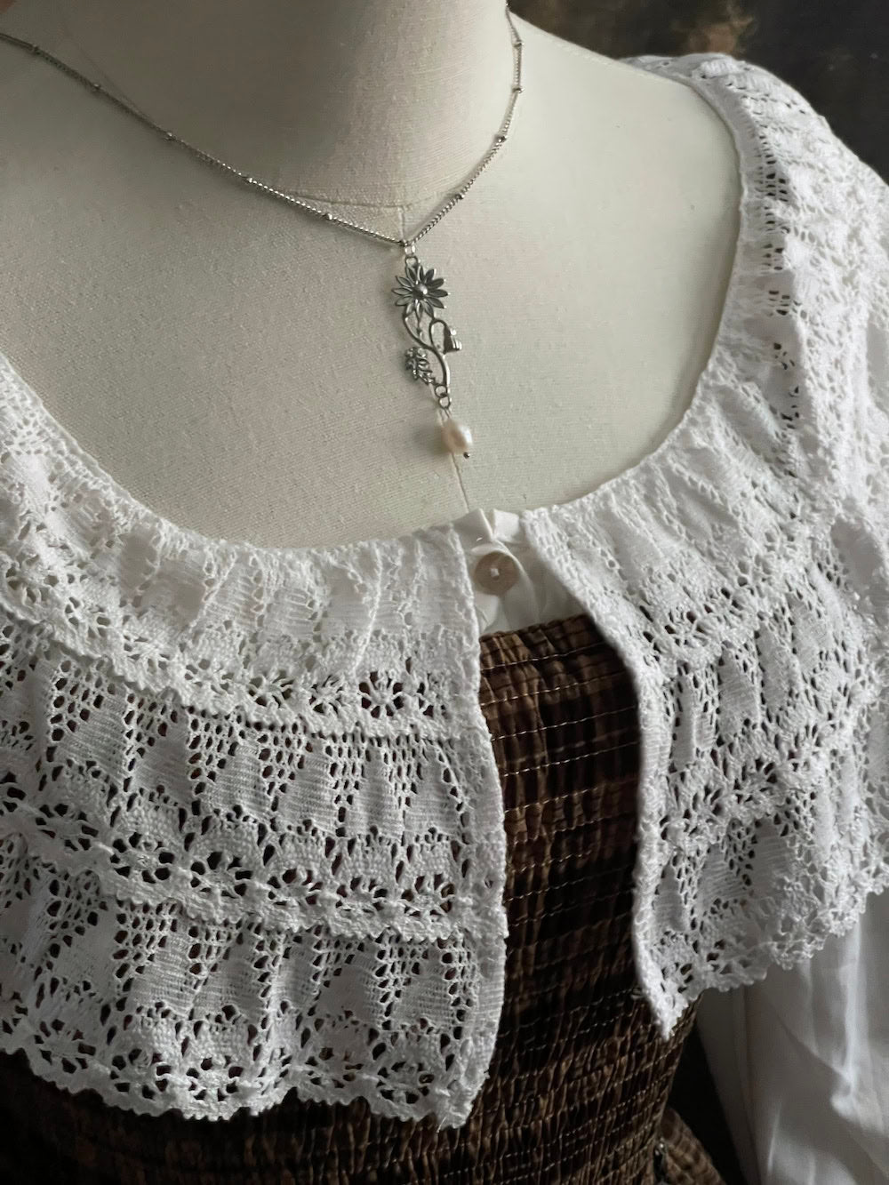 A mannequin wearing a historical jewelry inspired vintage style daisy flower pendant necklace with pearl dangle in silver toned stainless steel