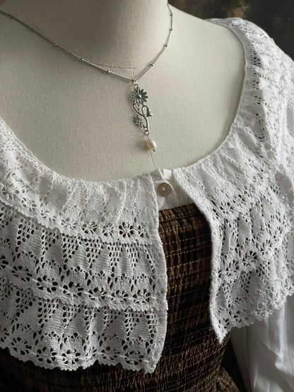A mannequin wearing a historical jewelry inspired vintage style daisy flower pendant necklace with pearl dangle in silver toned stainless steel