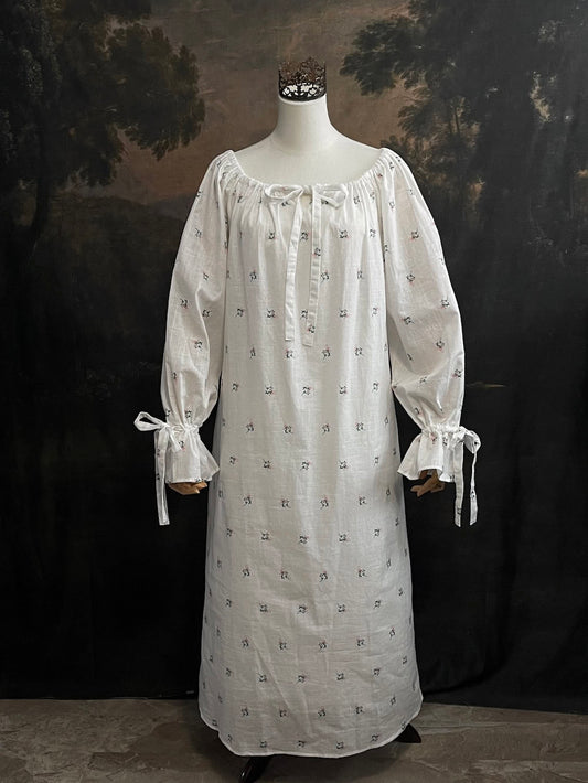 A historically inspired regency and victorian era chemise dress made of white floral printed cotton with bell sleeves and cinched bow neckline