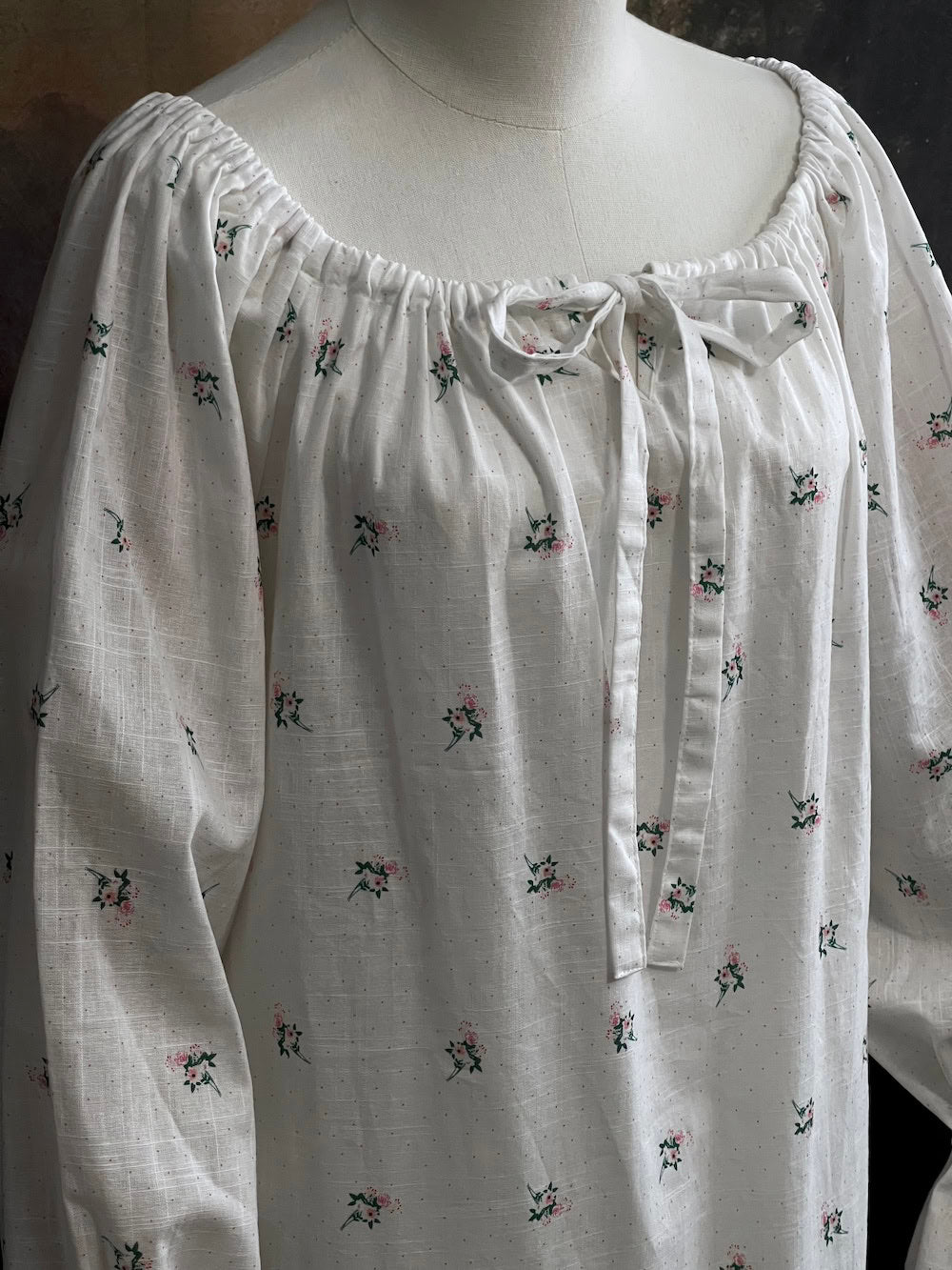 A historically inspired regency and victorian era chemise dress made of white floral printed cotton with bell sleeves and cinched bow neckline