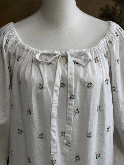 Close up of a historically inspired regency and victorian era chemise dress made of white floral printed cotton with bell sleeves and cinched bow neckline
