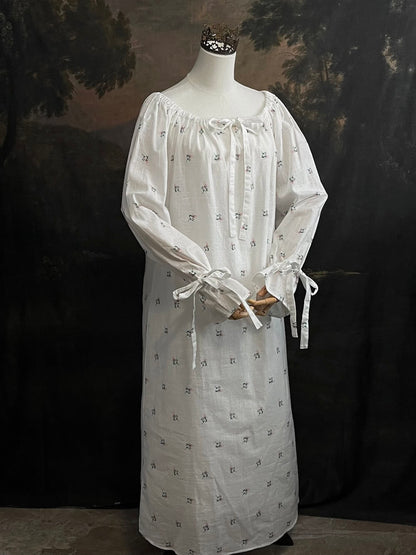 A historically inspired regency and victorian era chemise dress made of white floral printed cotton with bell sleeves and cinched bow neckline
