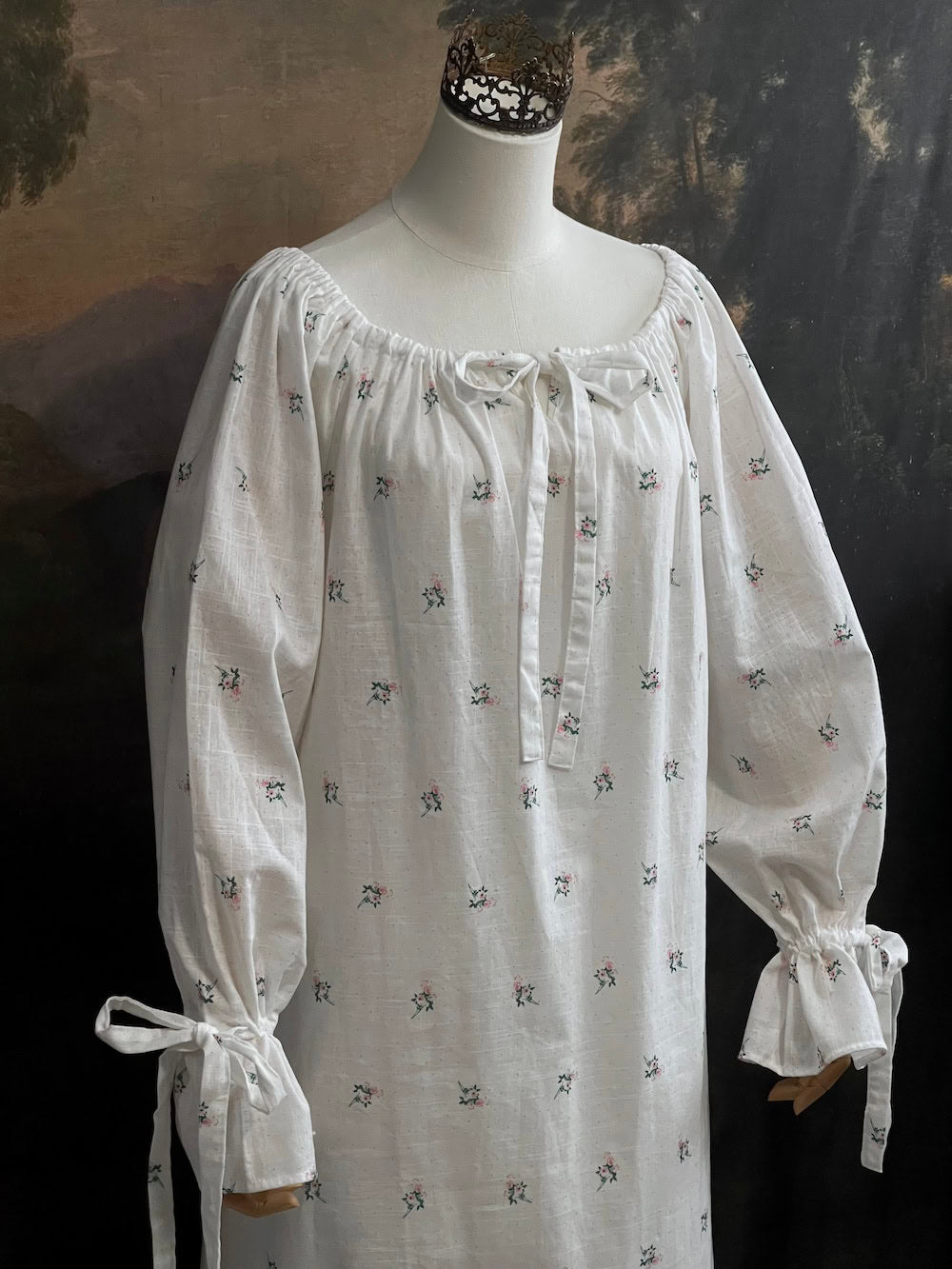 A historically inspired regency and victorian era chemise dress made of white floral printed cotton with bell sleeves and cinched bow neckline