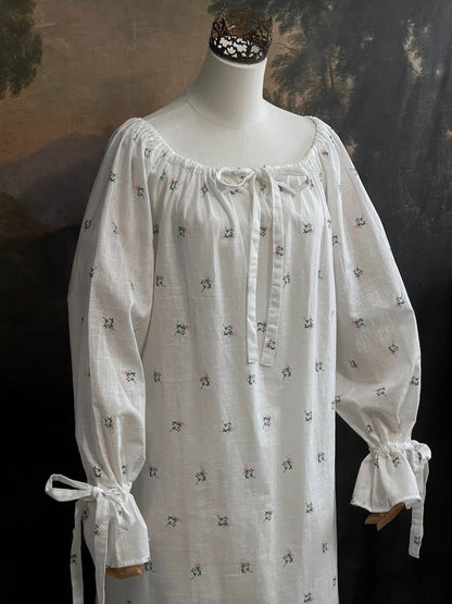 A historically inspired regency and victorian era chemise dress made of white floral printed cotton with bell sleeves and cinched bow neckline