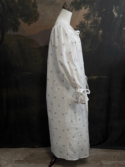 A historically inspired regency and victorian era chemise dress made of white floral printed cotton with bell sleeves and cinched bow neckline