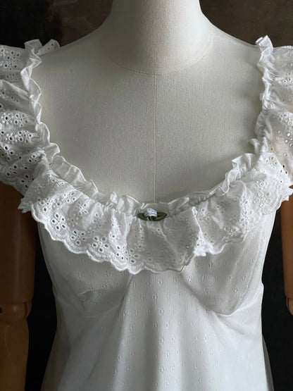 White Edwardian-inspired vintage style lace dress on a mannequin against a dark, forest-like art history background