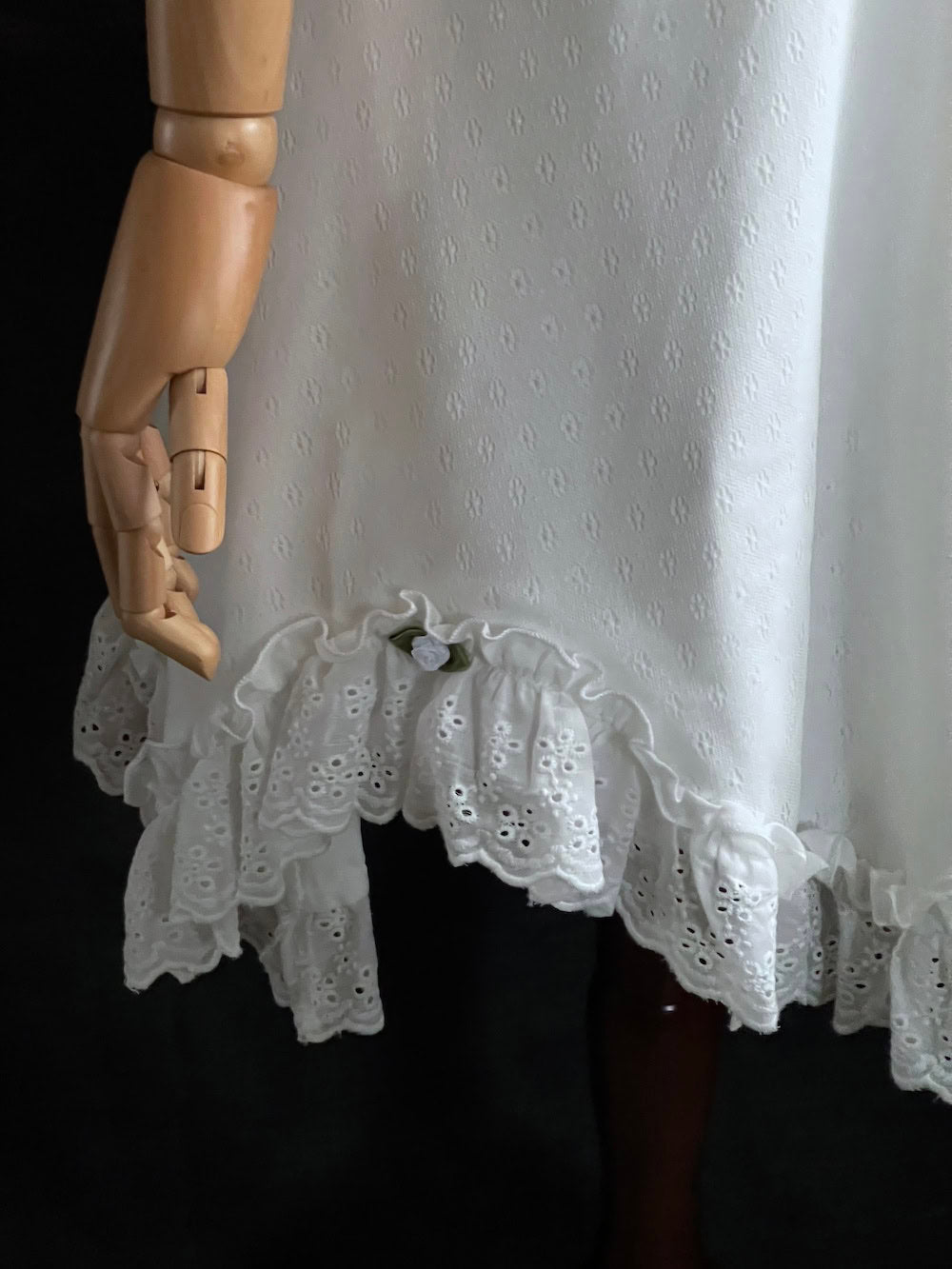 White Edwardian-inspired vintage style lace dress on a mannequin against a dark, forest-like art history background
