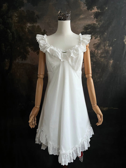 White Edwardian-inspired vintage style lace dress on a mannequin against a dark, forest-like art history background
