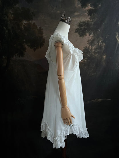 White Edwardian-inspired vintage style lace dress on a mannequin against a dark, forest-like art history background