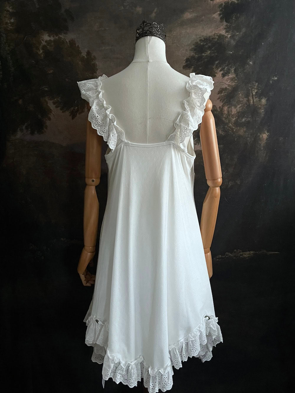 White Edwardian-inspired vintage style lace dress on a mannequin against a dark, forest-like art history background
