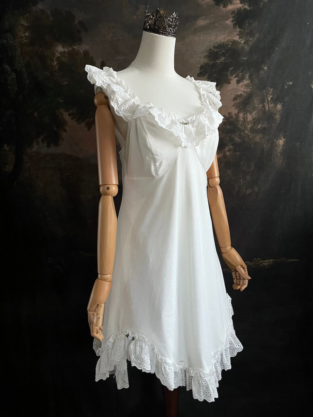 White Edwardian-inspired vintage style lace dress on a mannequin against a dark, forest-like art history background