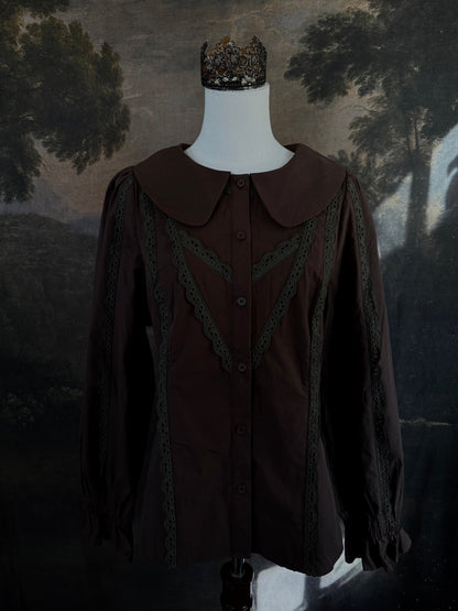 A historically inspired victorian era dark brown long-sleeve blouse with a large Peter Pan collar and lace trim details, displayed on a mannequin against a dark forest landscape backdrop.