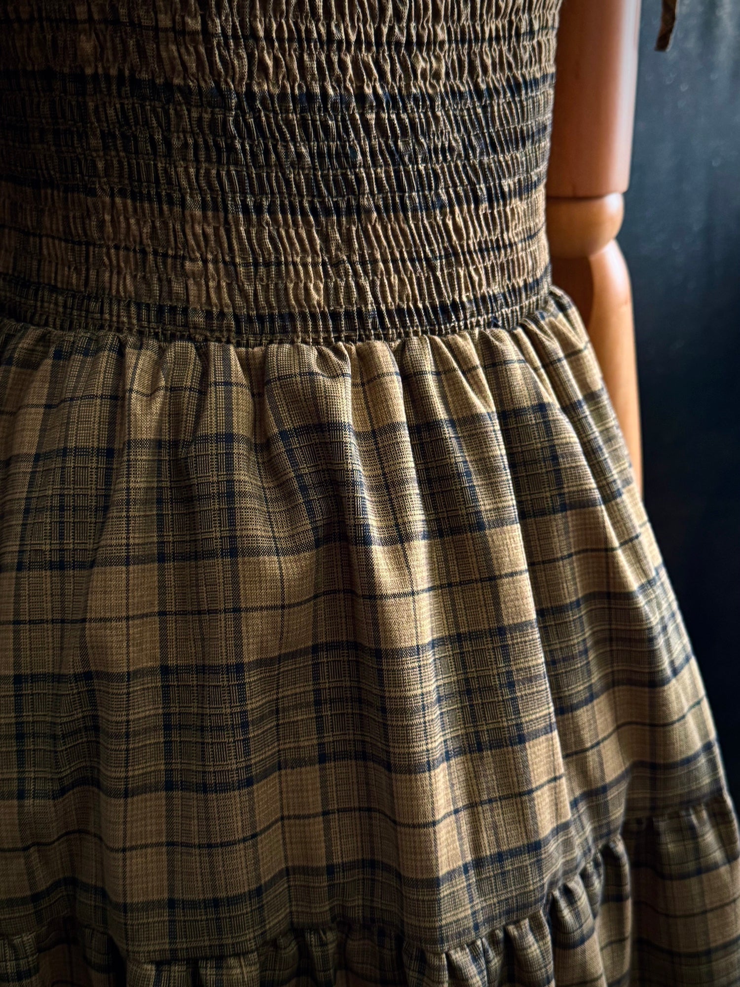 Close-up of an olive green smocked dress with tartan patterned fabric
