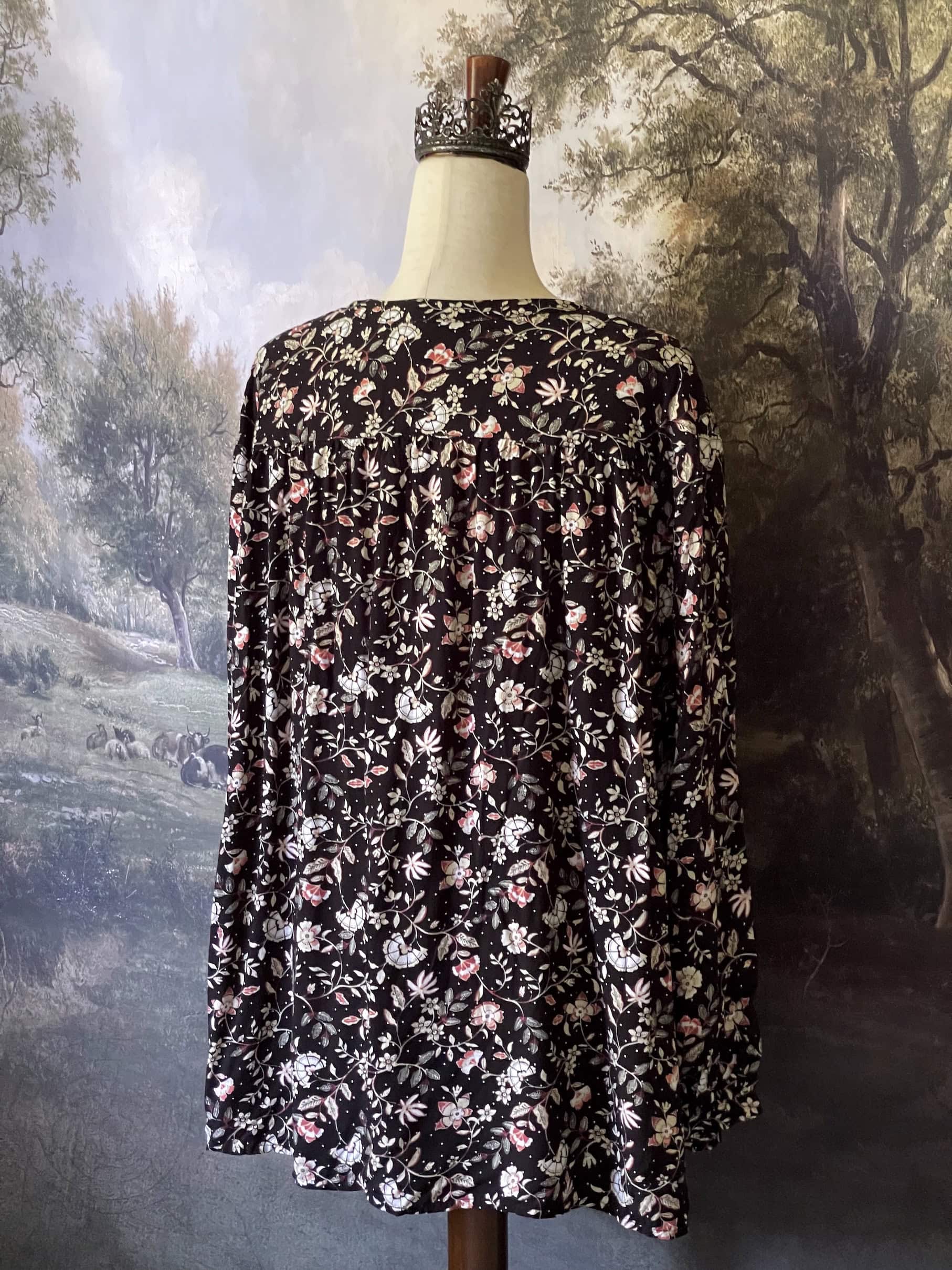 A Medieval Inspired Dark Botanical Print Blouse with Bishop Sleeves on a mannequin in front of a forested painting backdrop.