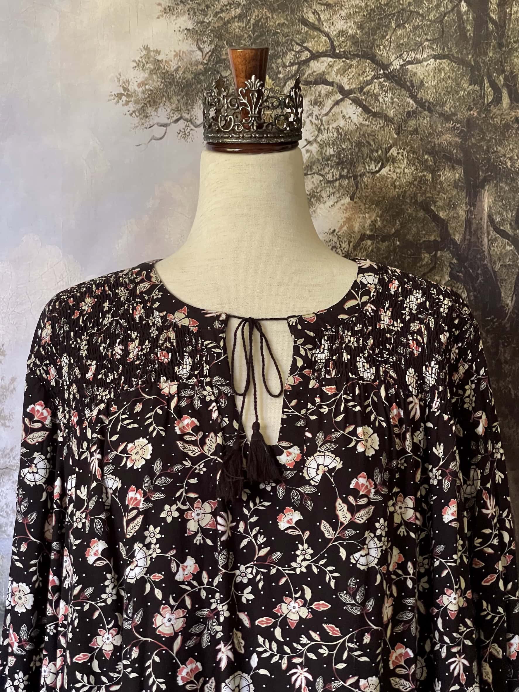 A Medieval Inspired Dark Botanical Print Blouse with Bishop Sleeves on a mannequin in front of a forested painting backdrop.