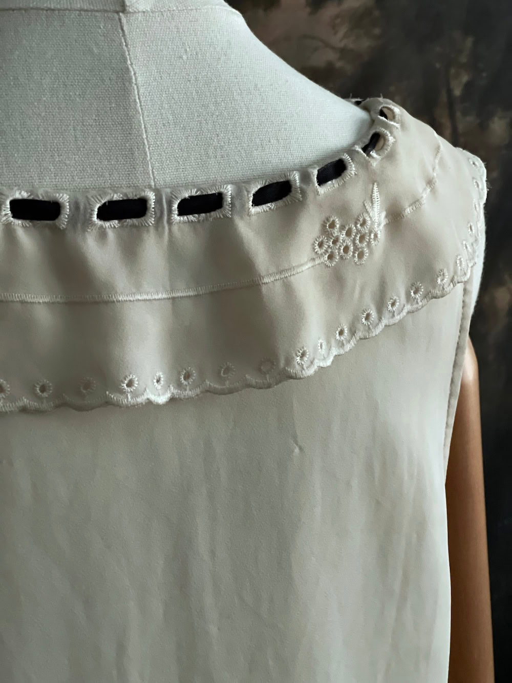 Close-up of a light-colored blouse with decorative trim on a blurred background