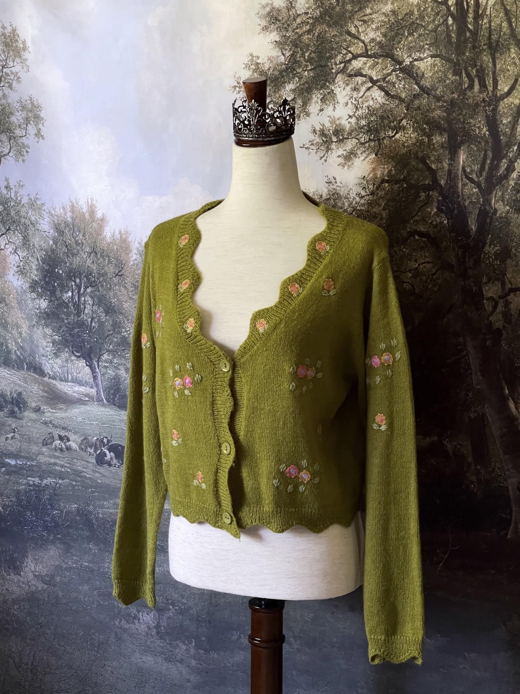 A cottagecore Historically Inspired chartreuse moss Green Knit Cardigan with Floral Embroidery on a mannequin in front of an art history backdrop.