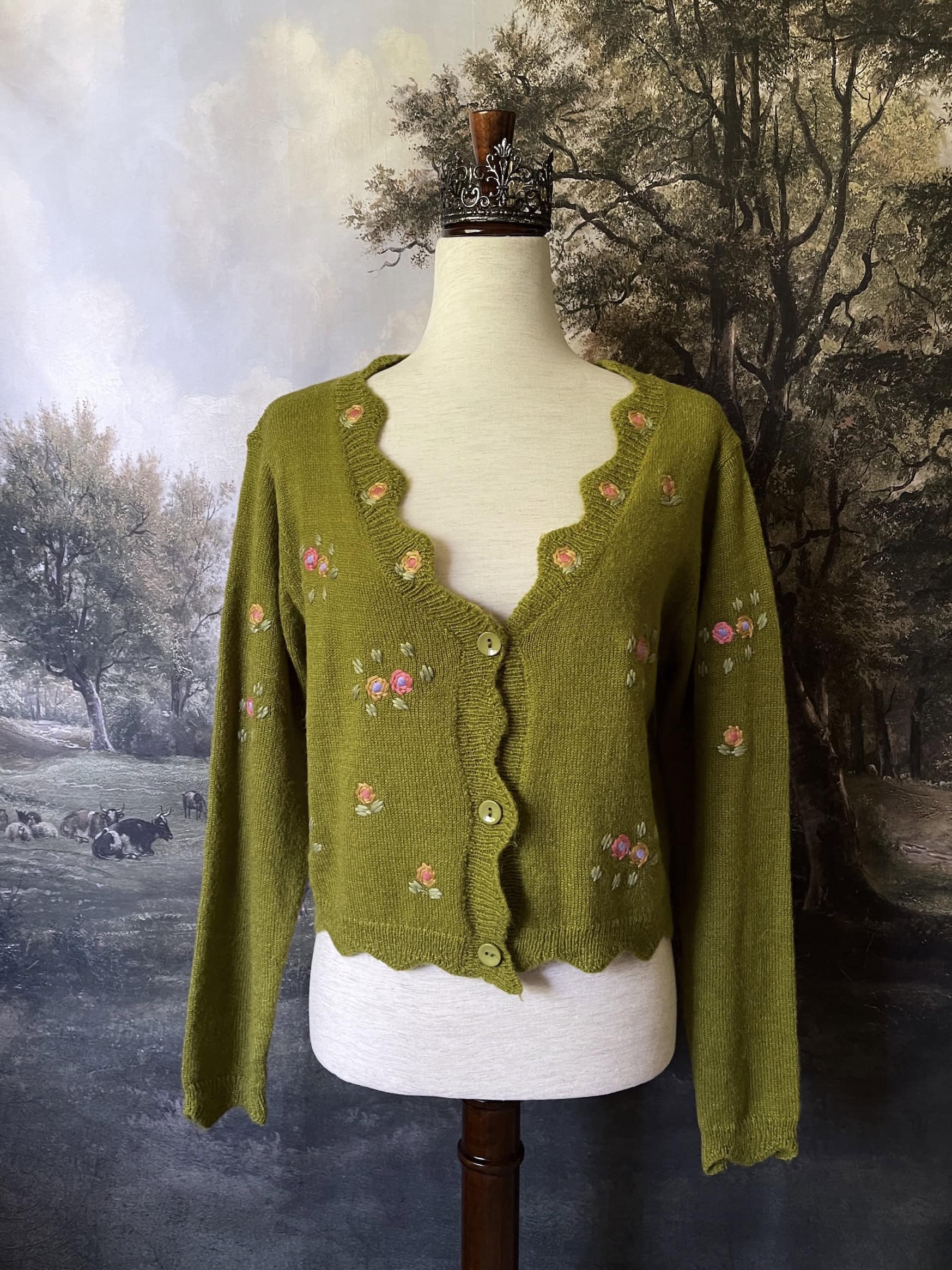 A cottagecore Historically Inspired chartreuse moss Green Knit Cardigan with Floral Embroidery on a mannequin in front of an art history backdrop.