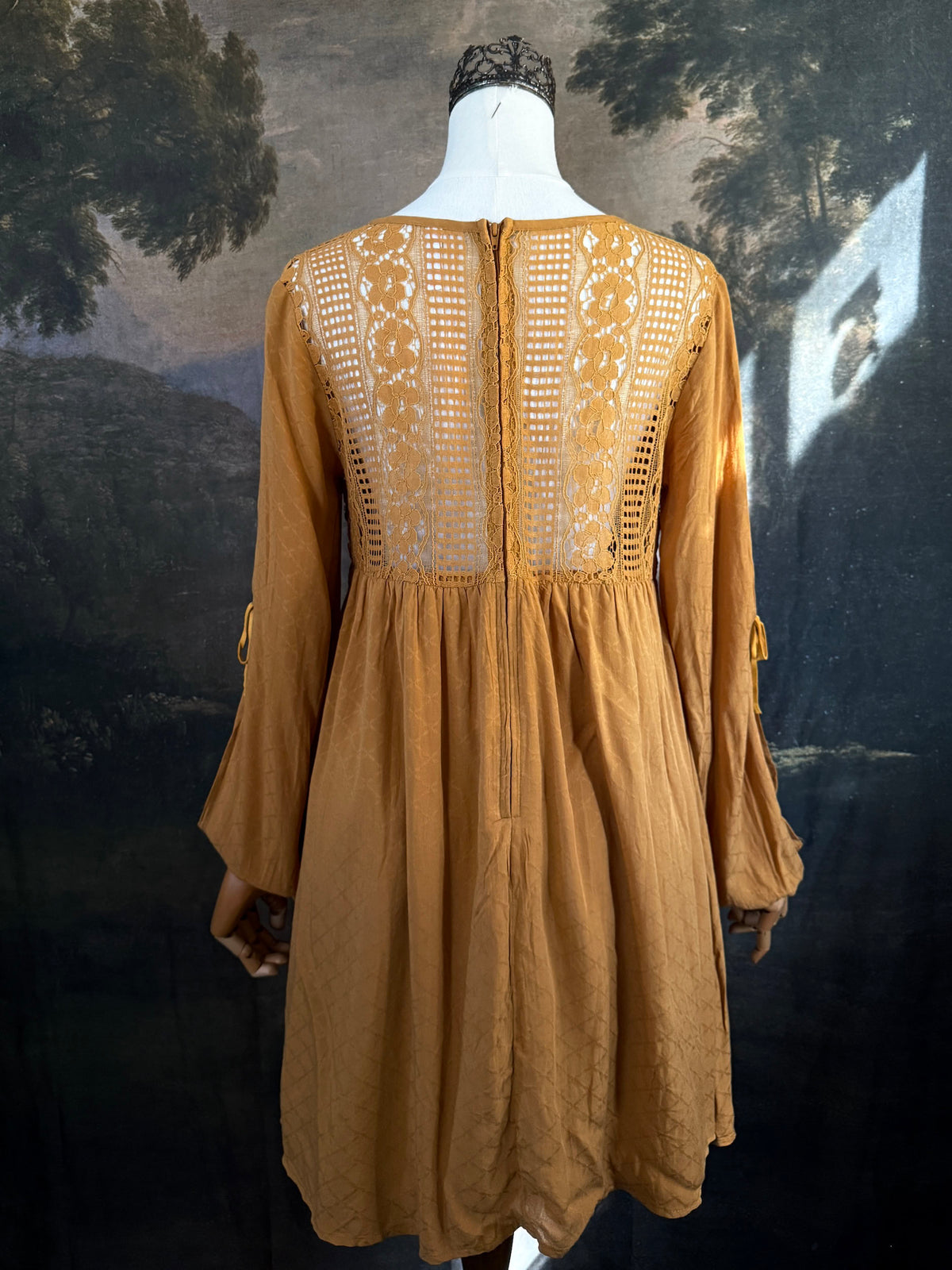 A medieval renaissance inspired tunic dress with cathedral arch lace, billowy slashed bishop sleeves, all in a golden yellow fabric. Pictured on a mannequin in front of a historical painting backdrop.