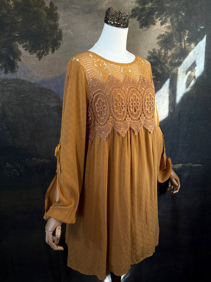 A medieval renaissance inspired tunic dress with cathedral arch lace, billowy slashed bishop sleeves, all in a golden yellow fabric. Pictured on a mannequin in front of a historical painting backdrop.