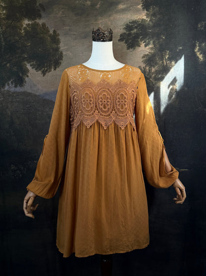 A medieval renaissance inspired tunic dress with cathedral arch lace, billowy slashed bishop sleeves, all in a golden yellow fabric. Pictured on a mannequin in front of a historical painting backdrop.