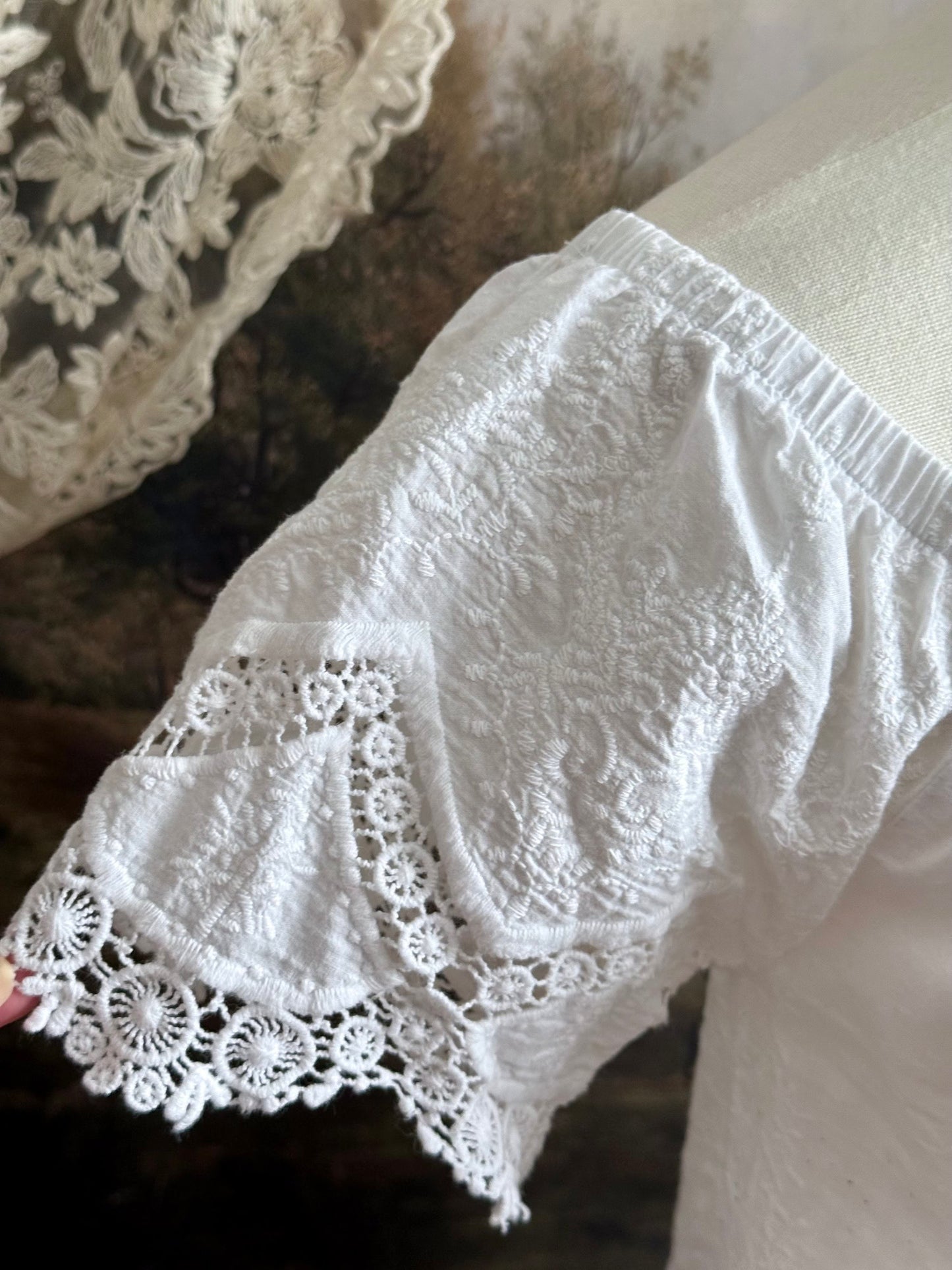 A historically inspired white embroidered peasant chemise blouse with short sleeves on a mannequin in front of an art history painting backdrop of a field