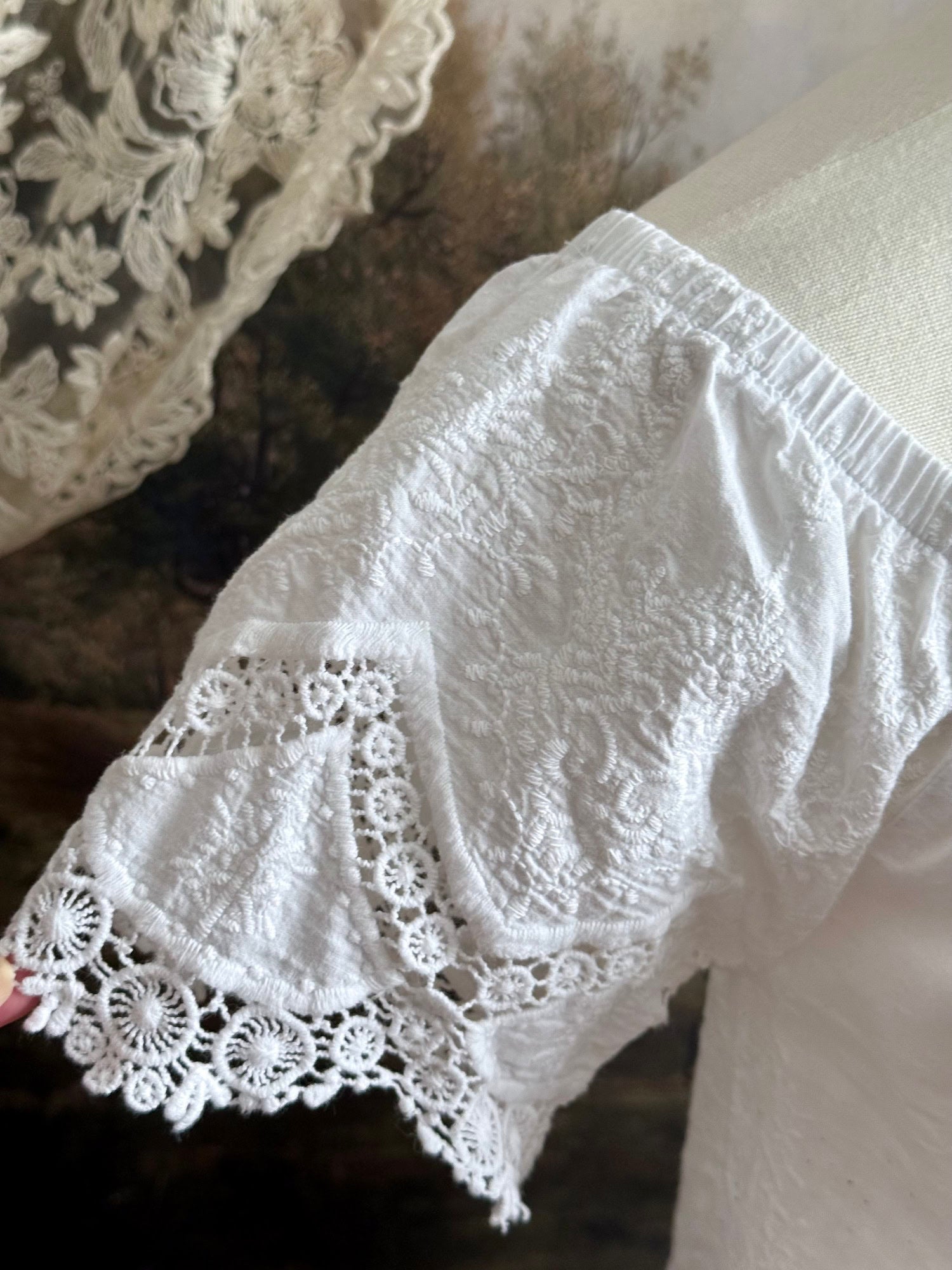 A historically inspired white embroidered peasant chemise blouse with short sleeves on a mannequin in front of an art history painting backdrop of a field