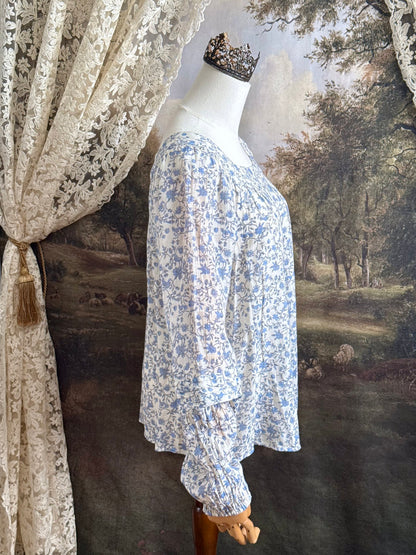 A white and blue historically inspired floral vine print blouse with square neckline and bishop sleeves, pictured on a mannequin in front of an art history backdrop