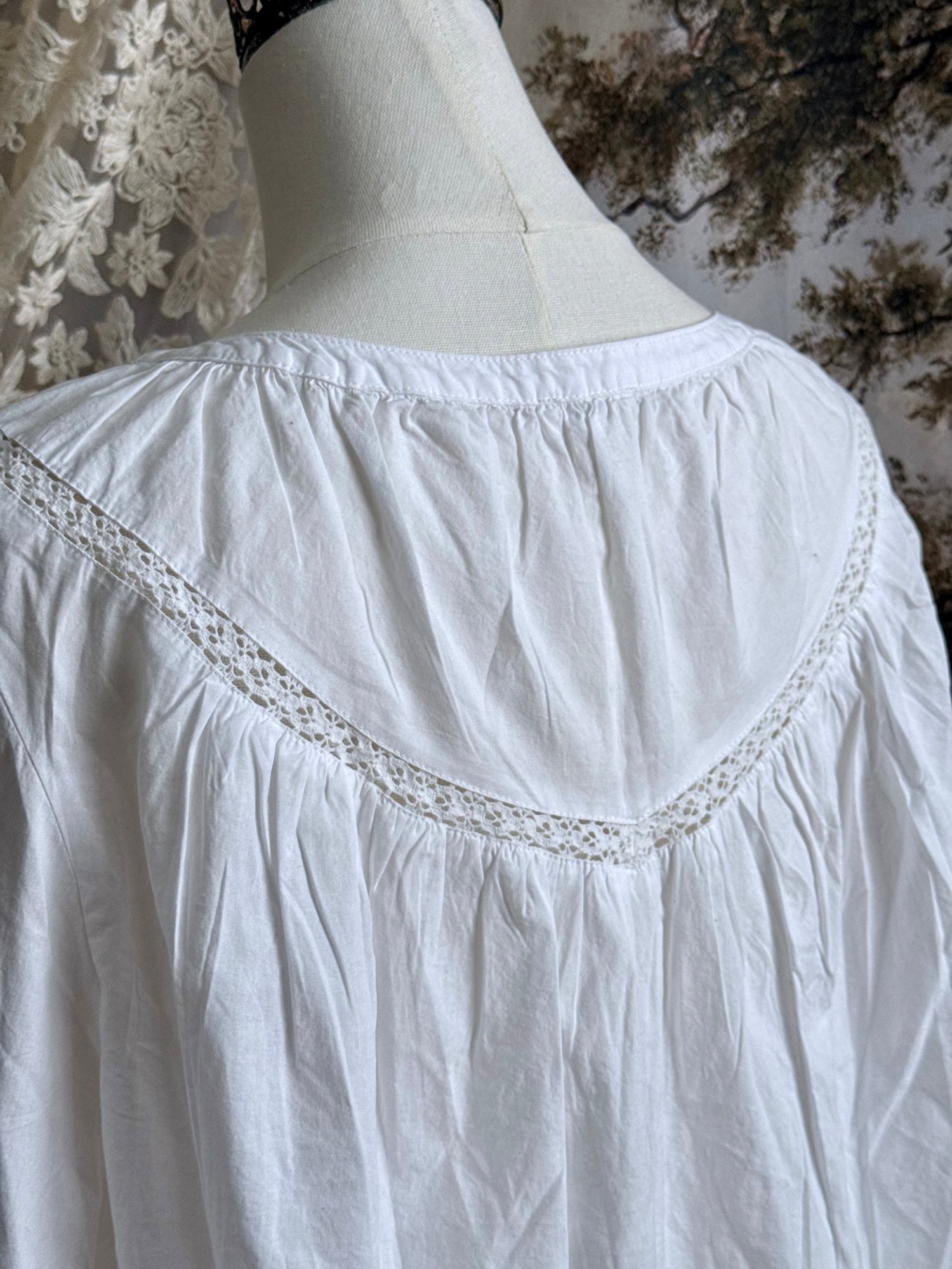 Historically inspired white cotton blouse with bishop sleeves, pintuck pleated details, lace trim, and a tie-front sillhouette. Pictured on a mannequin in front of an art history backdrop.