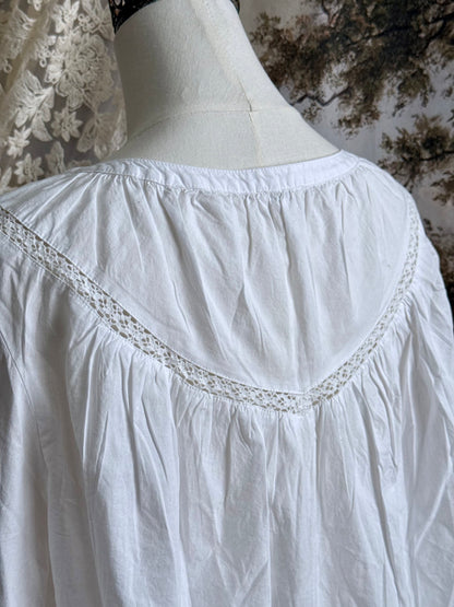 Historically inspired white cotton blouse with bishop sleeves, pintuck pleated details, lace trim, and a tie-front sillhouette. Pictured on a mannequin in front of an art history backdrop.