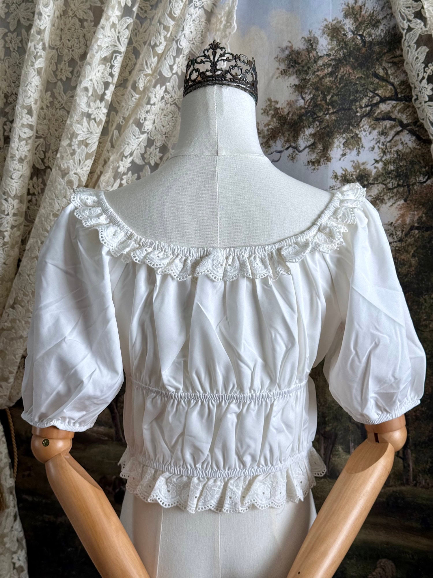 Historical fashion inspired vintage style white shirred top chemise with puff sleeves and floral lace trim on a mannequin in front of an art history backdrop and lace curtain.