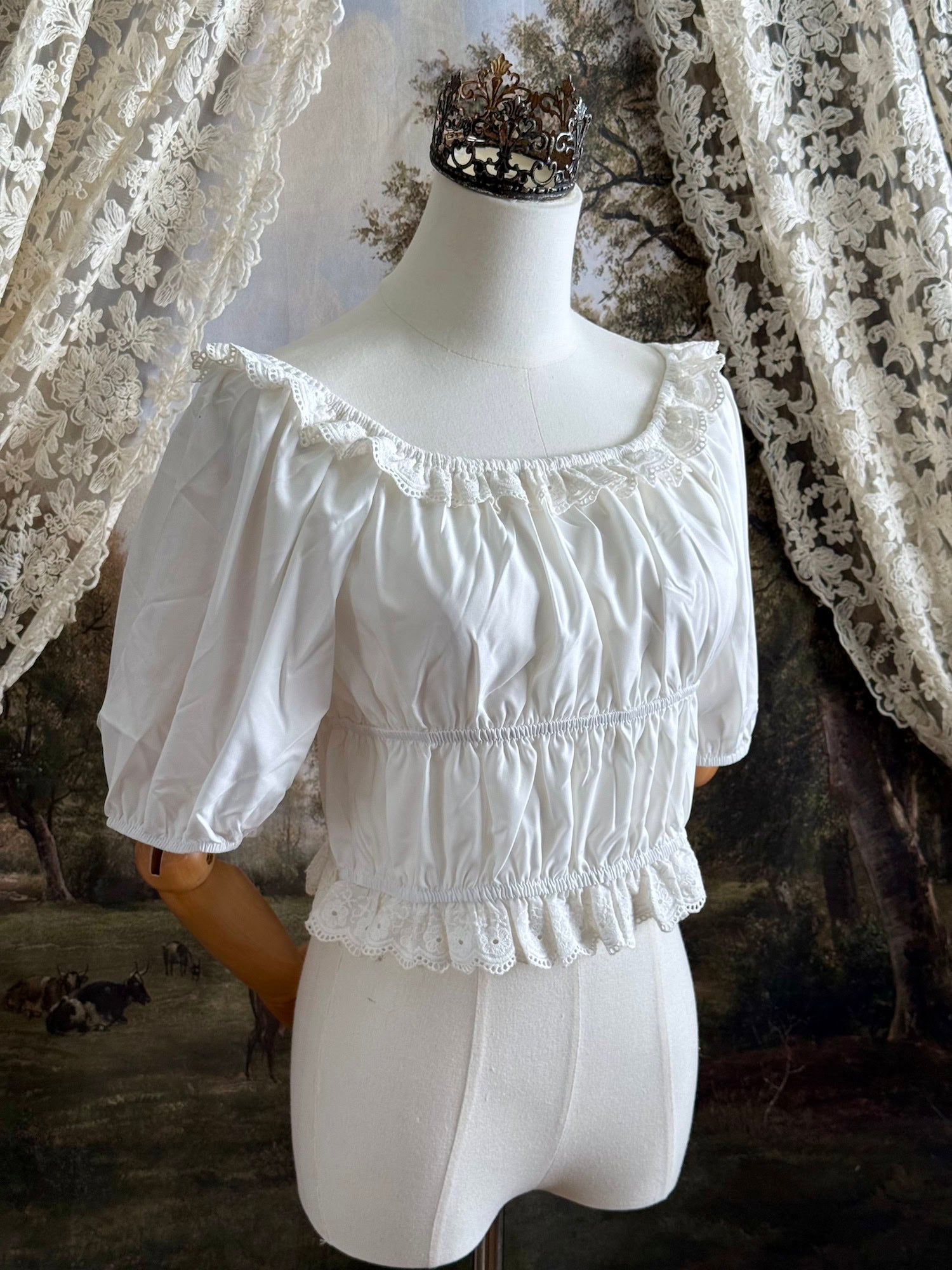 Historical fashion inspired vintage style white shirred top chemise with puff sleeves and floral lace trim on a mannequin in front of an art history backdrop and lace curtain.