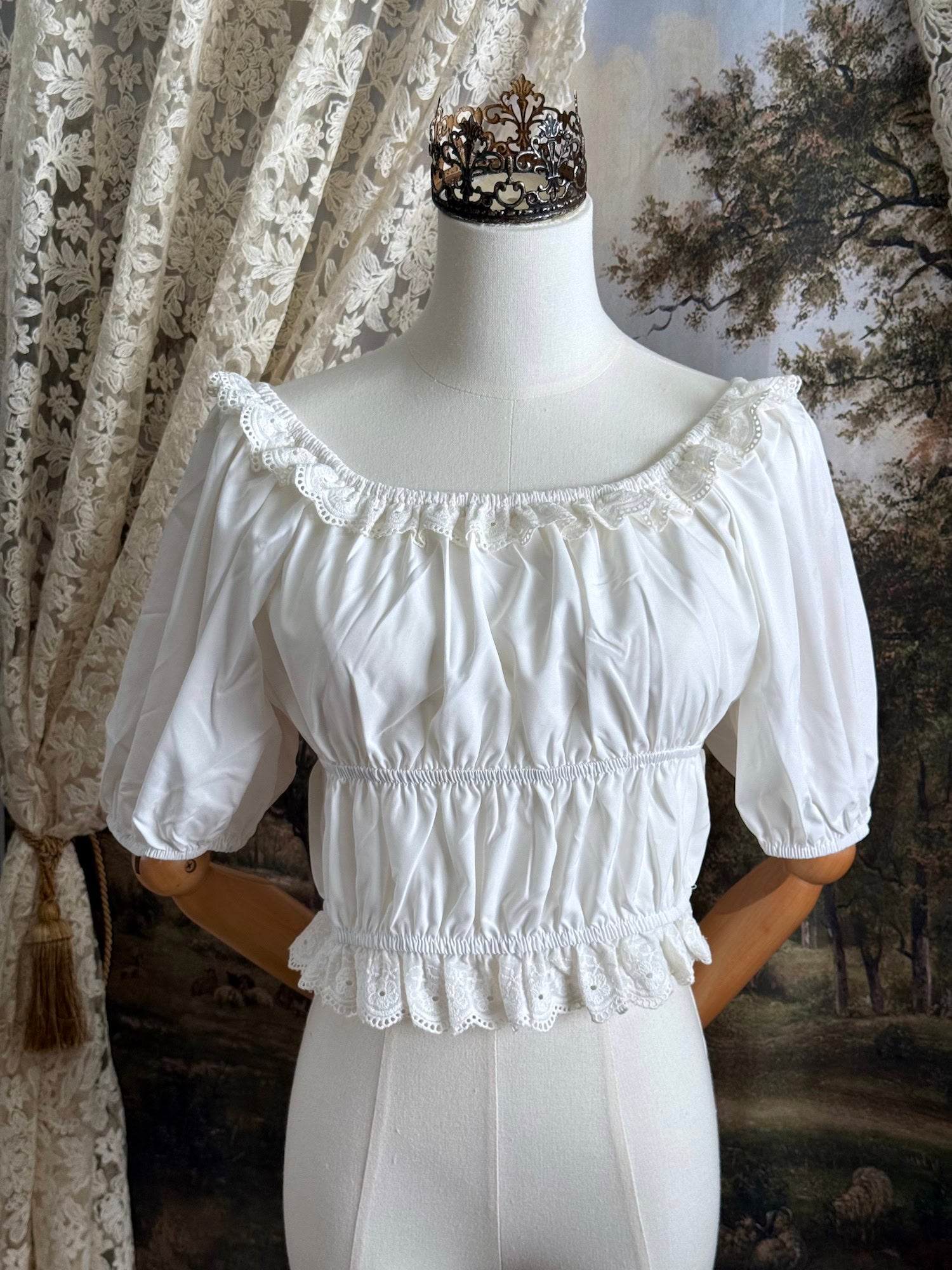 Historical fashion inspired vintage style white shirred top chemise with puff sleeves and floral lace trim on a mannequin in front of an art history backdrop and lace curtain.