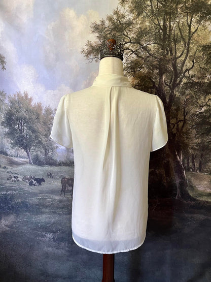 A historically inspired Vintage era Chiffon Button-up Blouse with Short Flutter Sleeves and a lace collar is pictured on a mannequin in front of an art history backdrop.